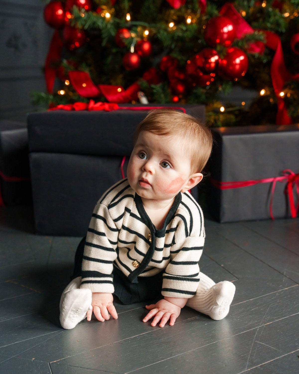 Christmas photo of a young baby in front of a Christmas tree and gifts.