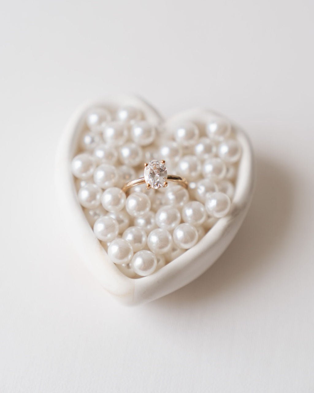 White Heart-shaped dish filled with pearls and a ring on a light background
