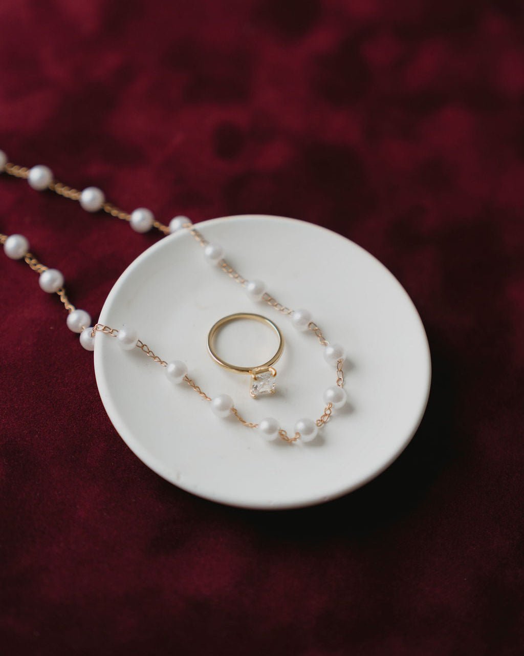 Maroon Pearl necklace and ring on a white dish with a red textured background