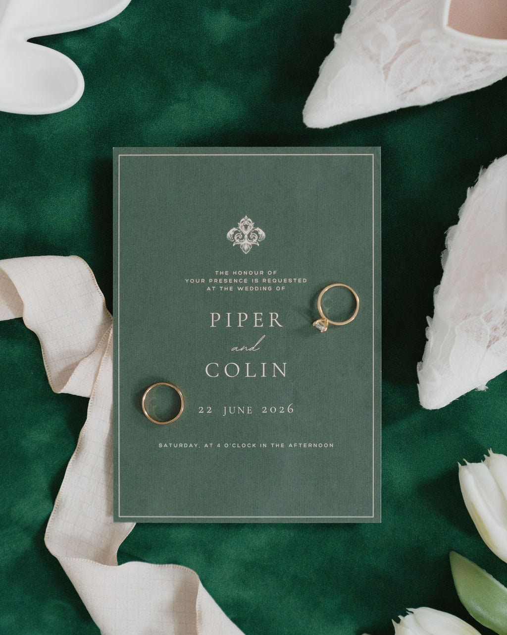 Wedding invitation card on a green matboard background with rings and white tulips.